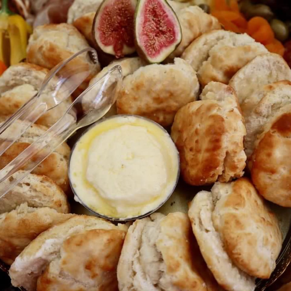 A platter of biscuits with a small bowl of butter, plastic tongs, and sliced figs.