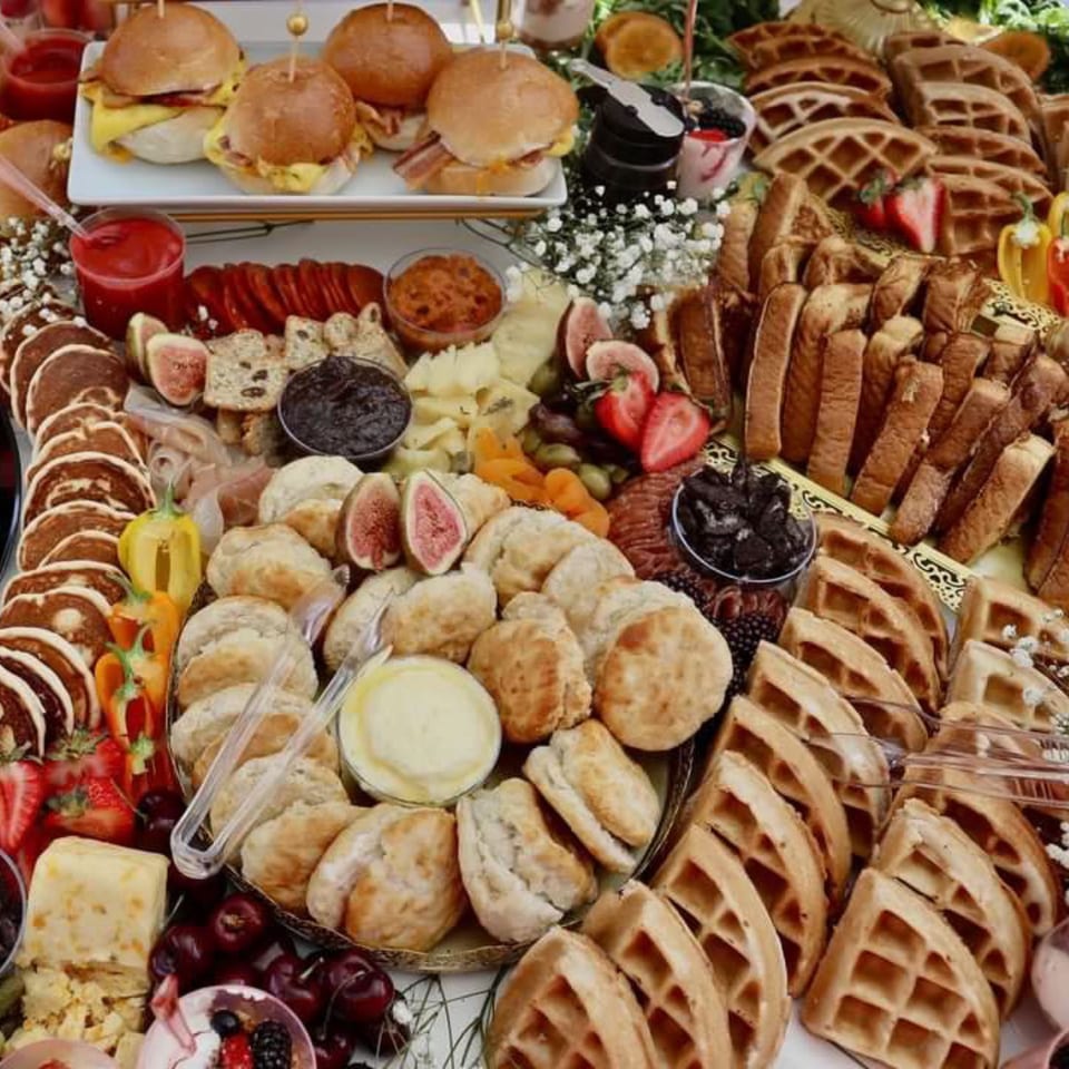 A lavish brunch spread featuring breakfast sliders, waffles, pancakes, biscuits, fruit, and cheeses.
