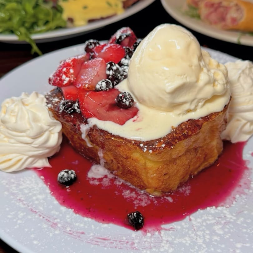 Golden French toast topped with strawberries, blueberries, vanilla ice cream, and whipped cream.